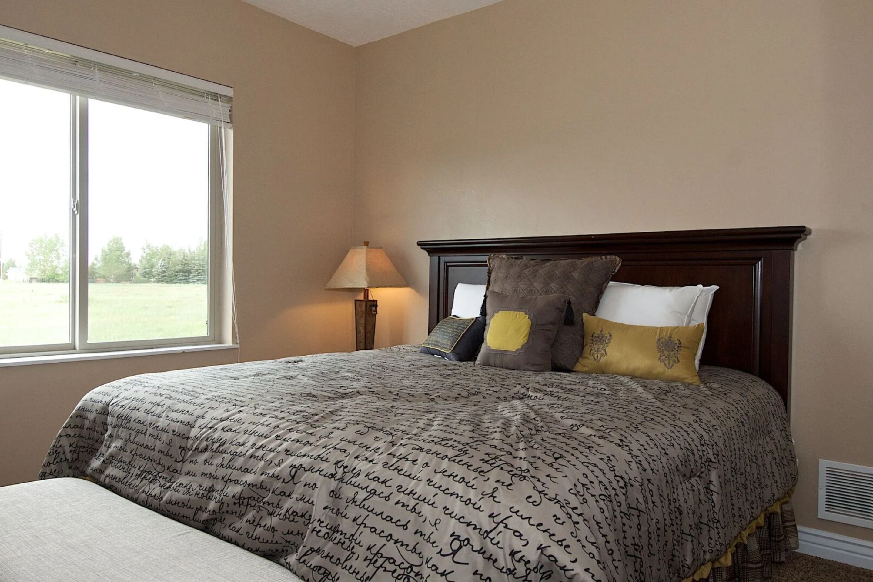 A bedroom with a large bed, a nightstand, a lamp, and a window with blinds.