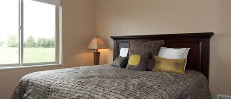 A bedroom with a large bed, a nightstand, a lamp, and a window with blinds.