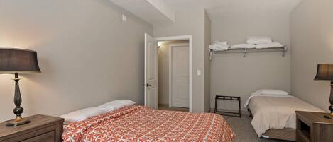 A bedroom with two beds, a nightstand with a lamp, a dresser, and a door leading to another room.