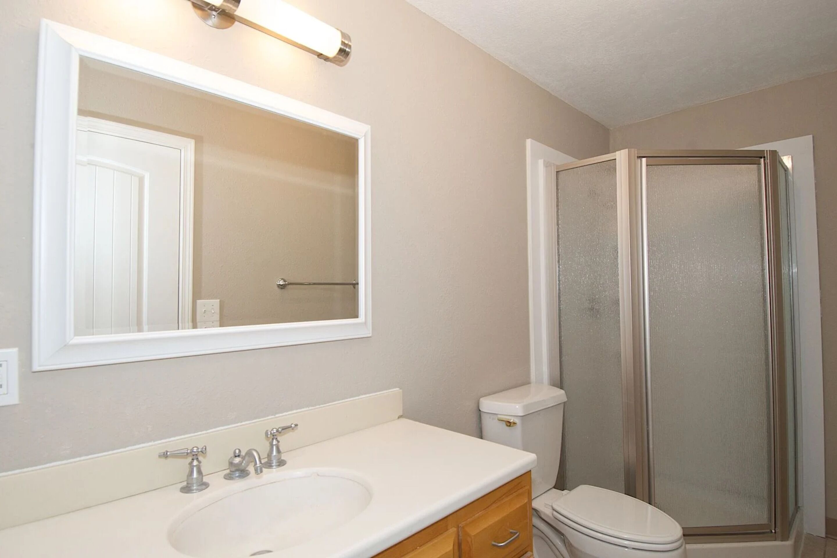 Une salle de bain avec un lavabo blanc, un miroir, des toilettes et une cabine de douche en verre.