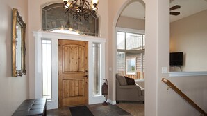 A foyer with a wooden door, a bench, a chandelier, and a staircase leading to another room. - Teton Harmony (Driggs)