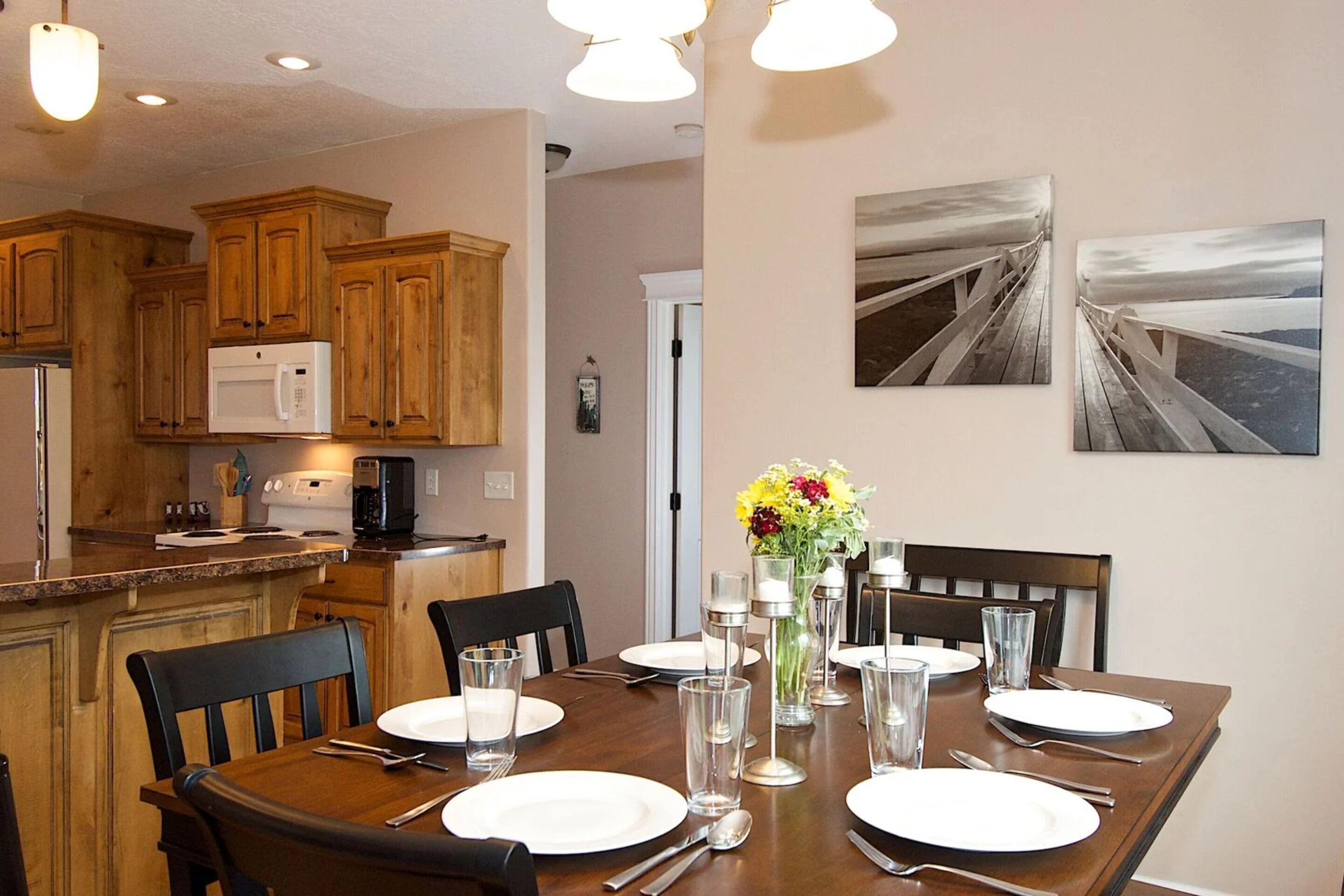 A dining area with a wooden table set for six, surrounded by chairs. There is a microwave and a coffee maker on the counter.