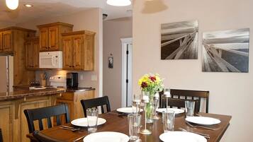 A dining area with a wooden table set for six, surrounded by chairs. There is a microwave and a coffee maker on the counter.