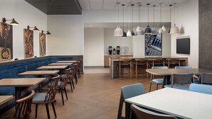 Un restaurante moderno con mesas y sillas de madera, un área de descanso con un banco acolchado azul e iluminación colgante.