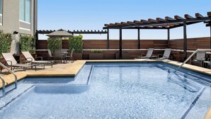 Un área de piscina en la azotea con sillones de descanso, una pérgola y una terraza de madera.