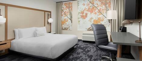 A hotel room with a large bed, a desk, a chair, and a TV.