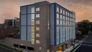Un hotel moderno con fachada de ladrillo y grandes ventanales. Tiene techo plano y se encuentra en una zona urbana con otros edificios alrededor.