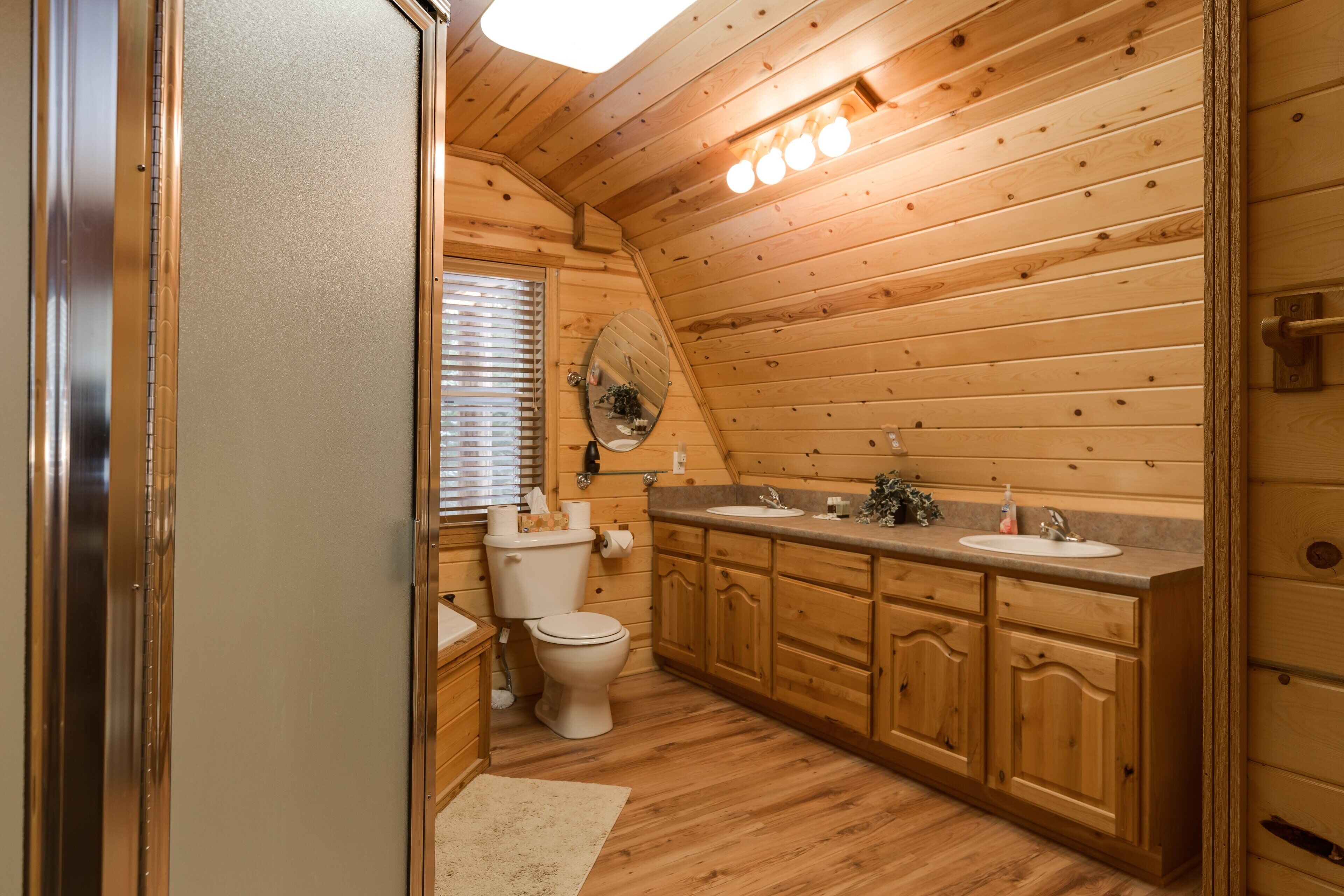 Une salle de bain de style rustique, avec des murs en bois, comprenant des toilettes, un lavabo et des placards.