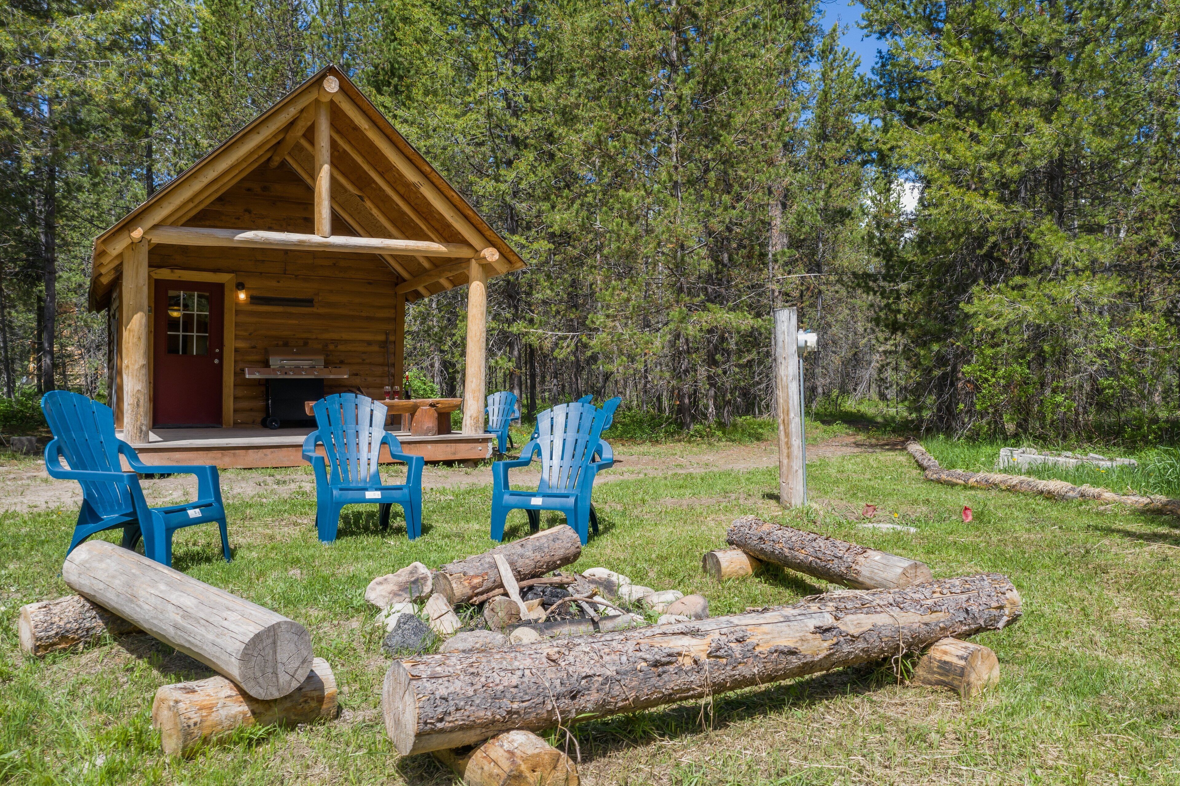 Un chalet rustique doté d’une véranda, de chaises Adirondack bleues et d’un foyer extérieur.