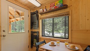 L’intérieur d’un chalet en bois comprend une table à manger, des chaises, une fenêtre donnant sur les arbres et une étagère avec des boîtes.