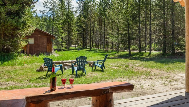 Une terrasse en bois avec une table dressée pour deux personnes, donnant sur une zone boisée où l’on aperçoit une petite cabane au loin.