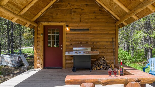 A wooden cabin with a barbecue grill, a table with glasses and a bottle, and a door with a window. - Little Fox (Island Park)