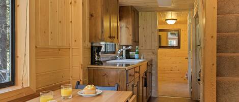 A wooden cabin interior with a kitchen area, a dining table with muffins and juice, and a staircase leading to another room.