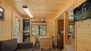 A wooden cabin interior with a sofa, dining table, chairs, a TV, and a staircase. - Little Fox (Island Park)