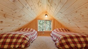 Une chambre mansardée chaleureuse, avec deux lits, une fenêtre et un plafond en bois.