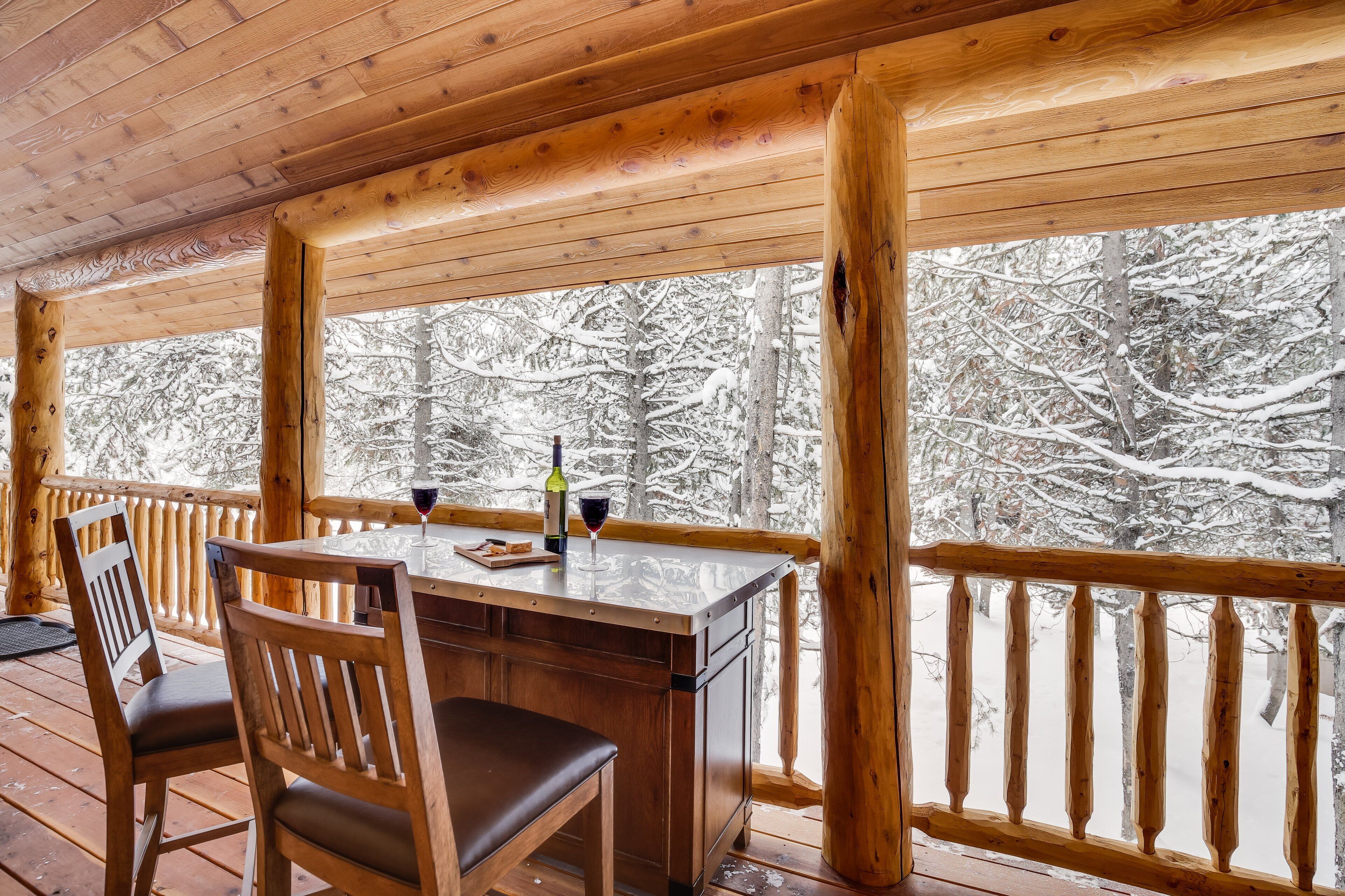 A wooden deck with a table and chairs, overlooking a snowy forest.