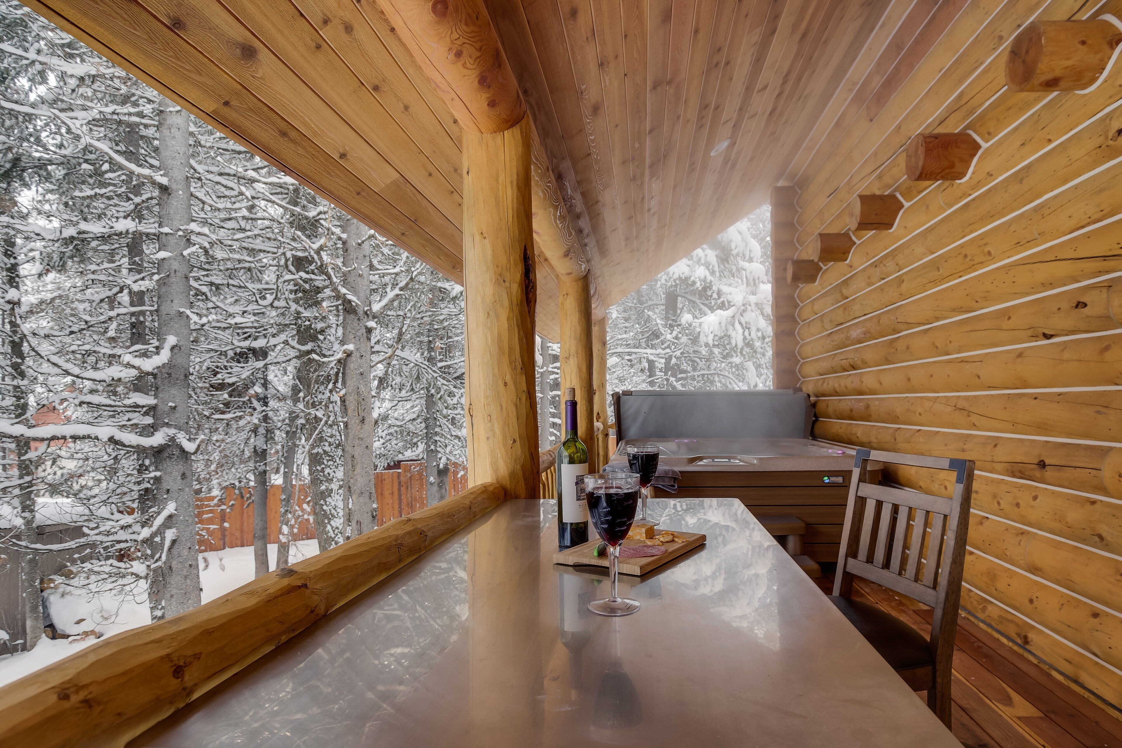 A wooden cabin with a table, two glasses of red wine, a bottle, and a plate of food.