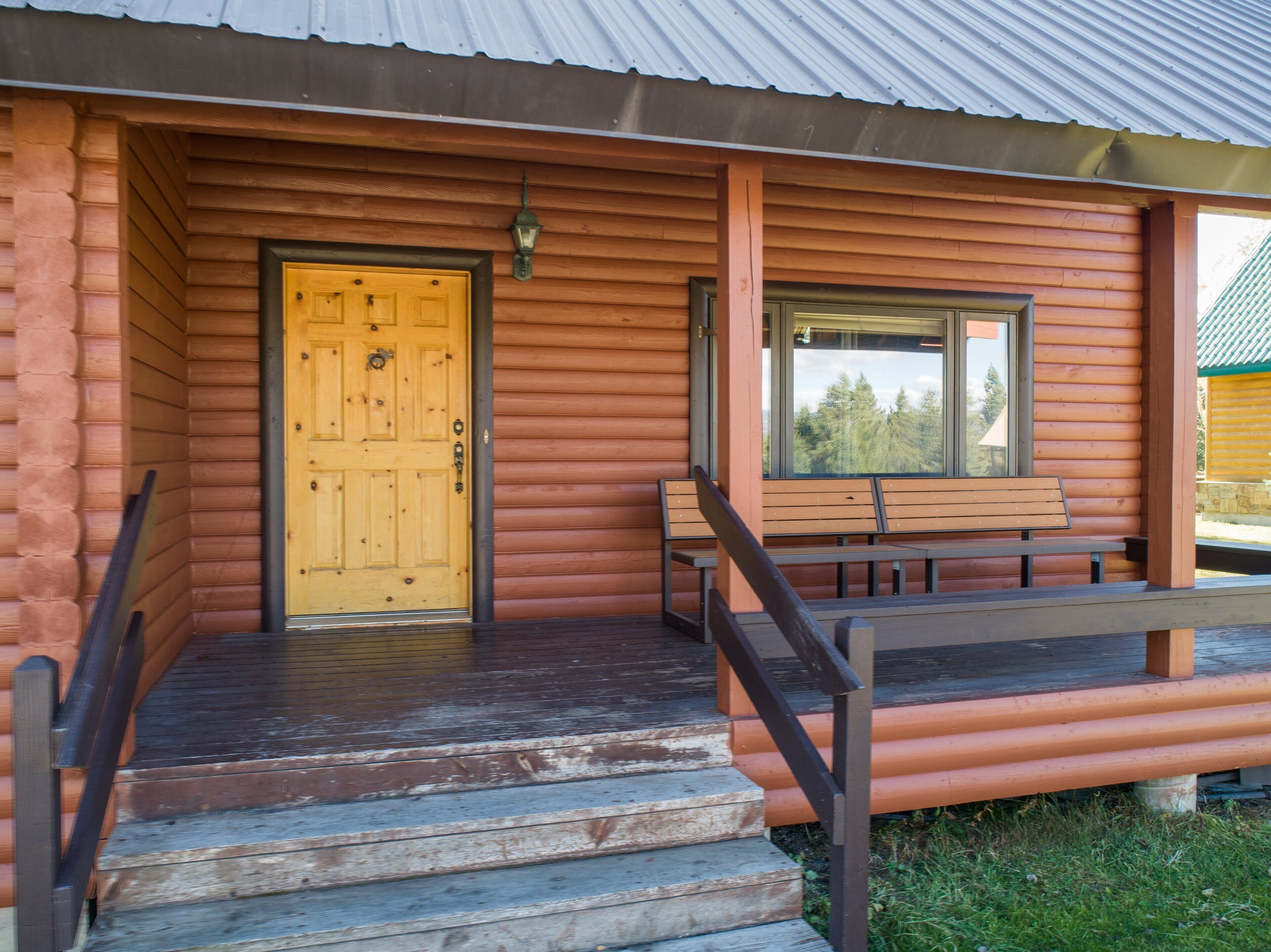 A wooden cabin with a yellow door, a bench, and a window overlooking a forest.