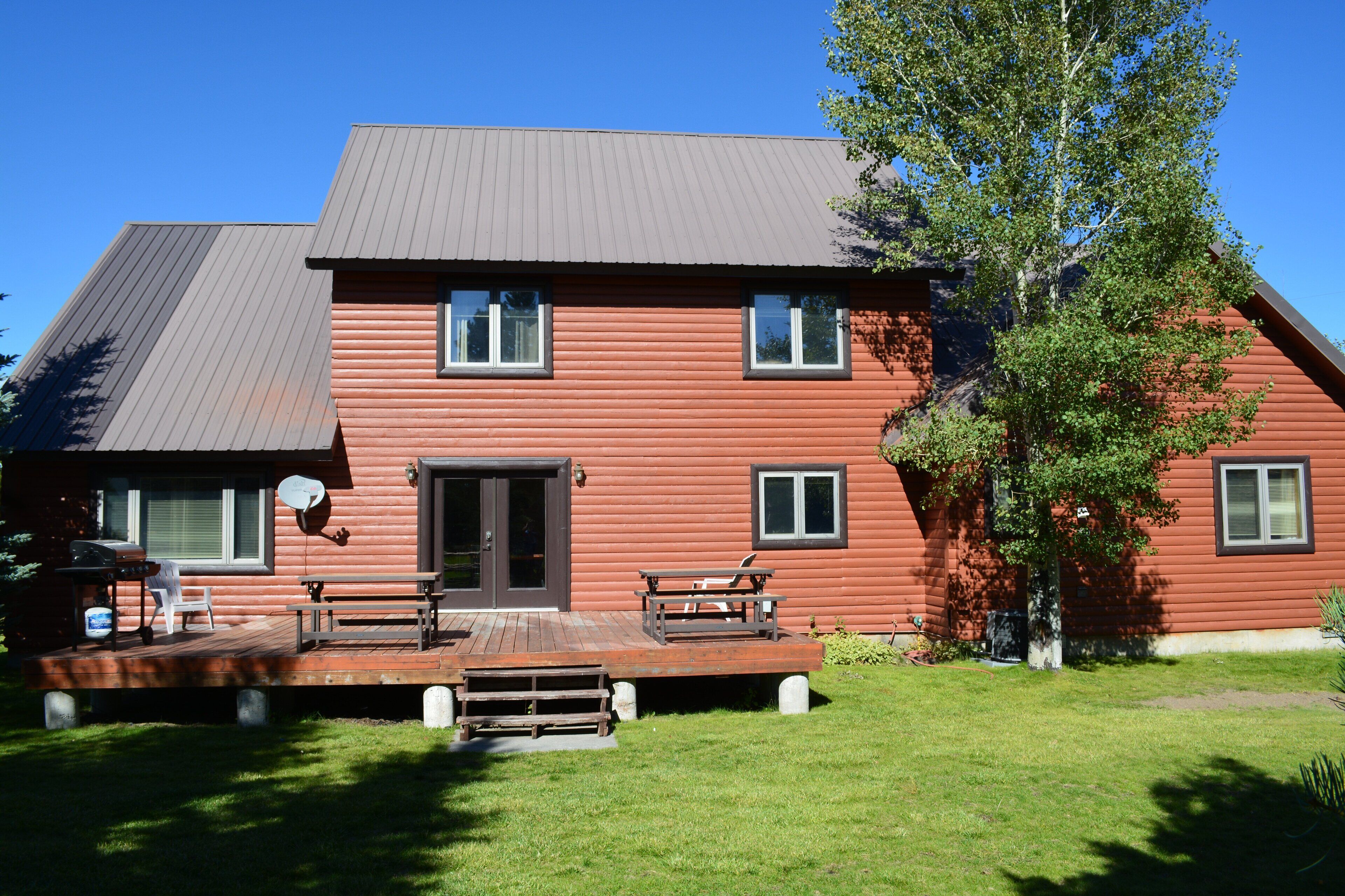 A two-story log cabin with a deck, a satellite dish, and a door with a window.