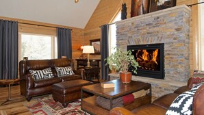 A cozy living room with a stone fireplace, leather furniture, and a large window with curtains. - Eagles Perch (Island Park)