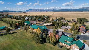An aerial view of a residential area with houses, green lawns, and a mountainous backdrop. - Eagles Perch (Island Park)