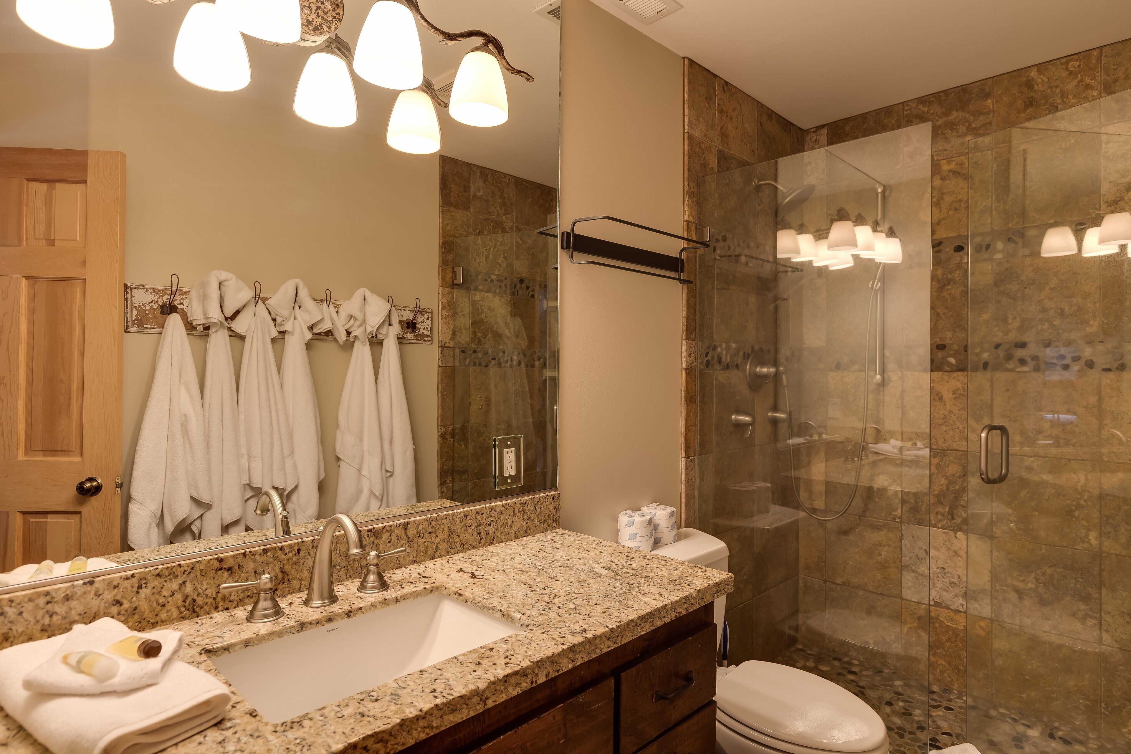 A modern bathroom with a granite countertop sink, a large mirror, and a glass-enclosed shower.