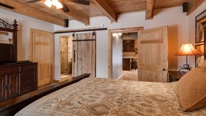 A bedroom with a large bed, wooden ceiling beams, a ceiling fan, and a sliding barn-style door. - Eagles Perch (Island Park)