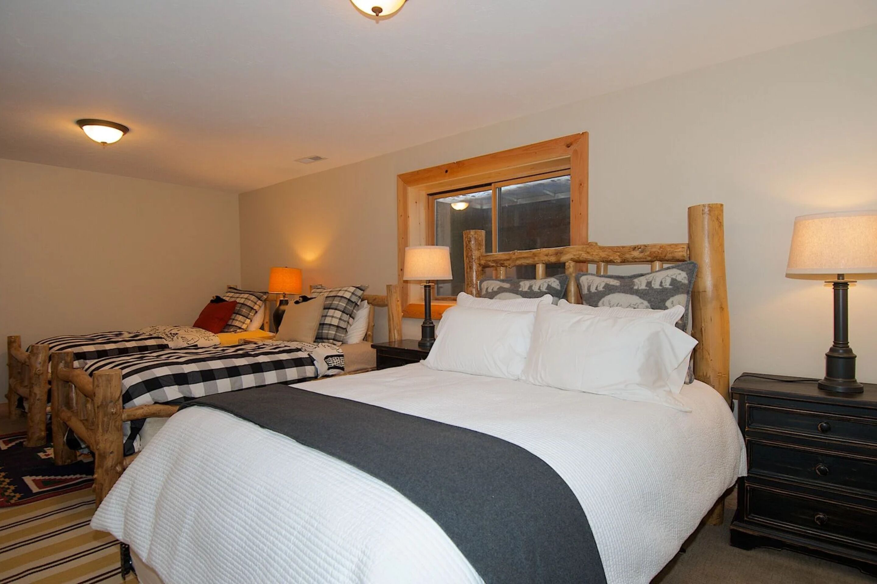 A bedroom with a large bed, two bedside tables, a nightstand, and a window with a wooden frame.