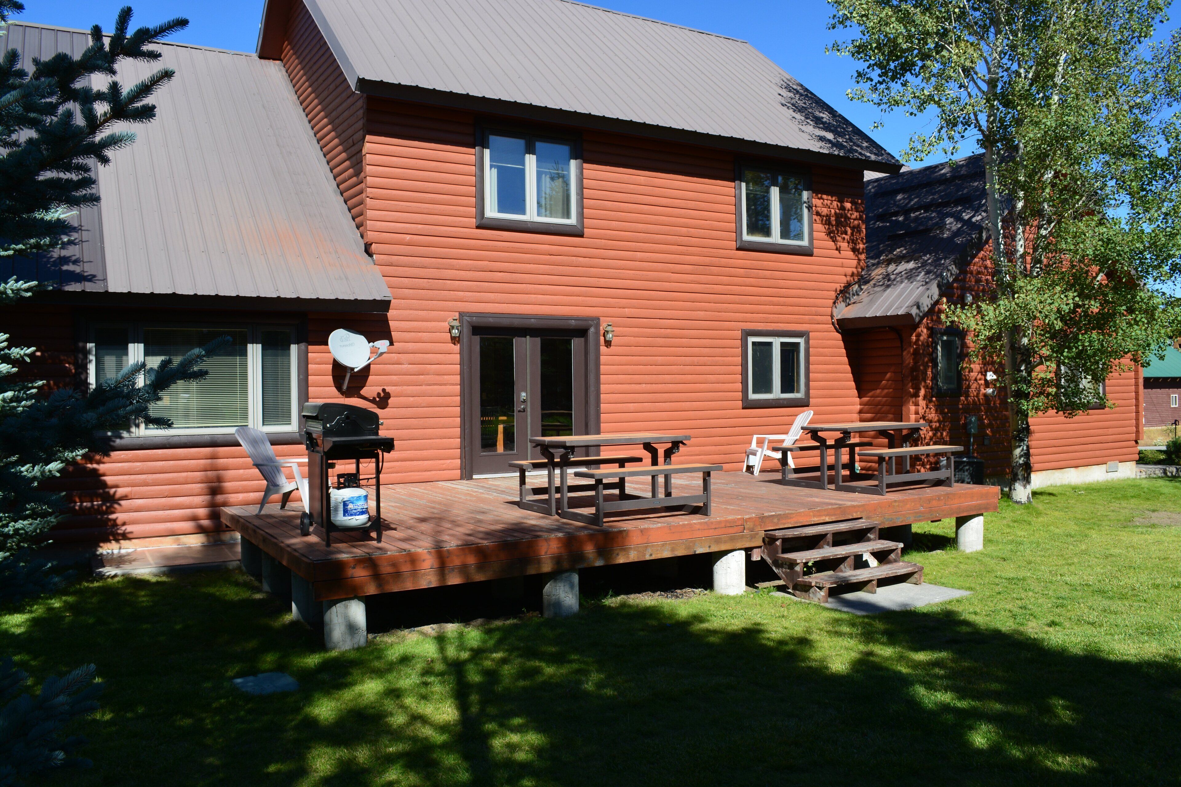 A two-story log cabin with a wooden deck, picnic tables, and a grill.