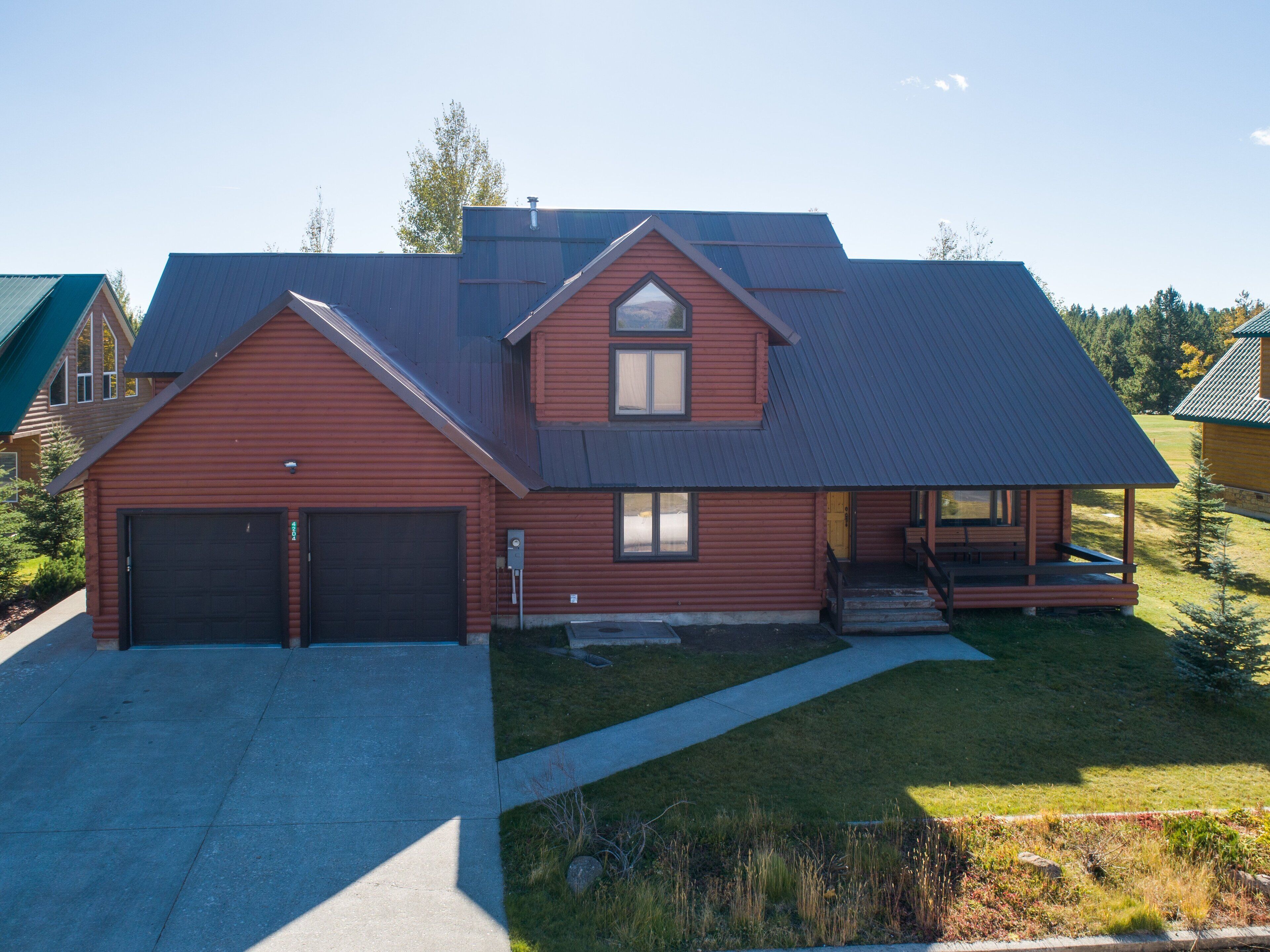 Eine zweistöckige Blockhütte mit Garage, überdachter Veranda und gepflegtem Rasen.