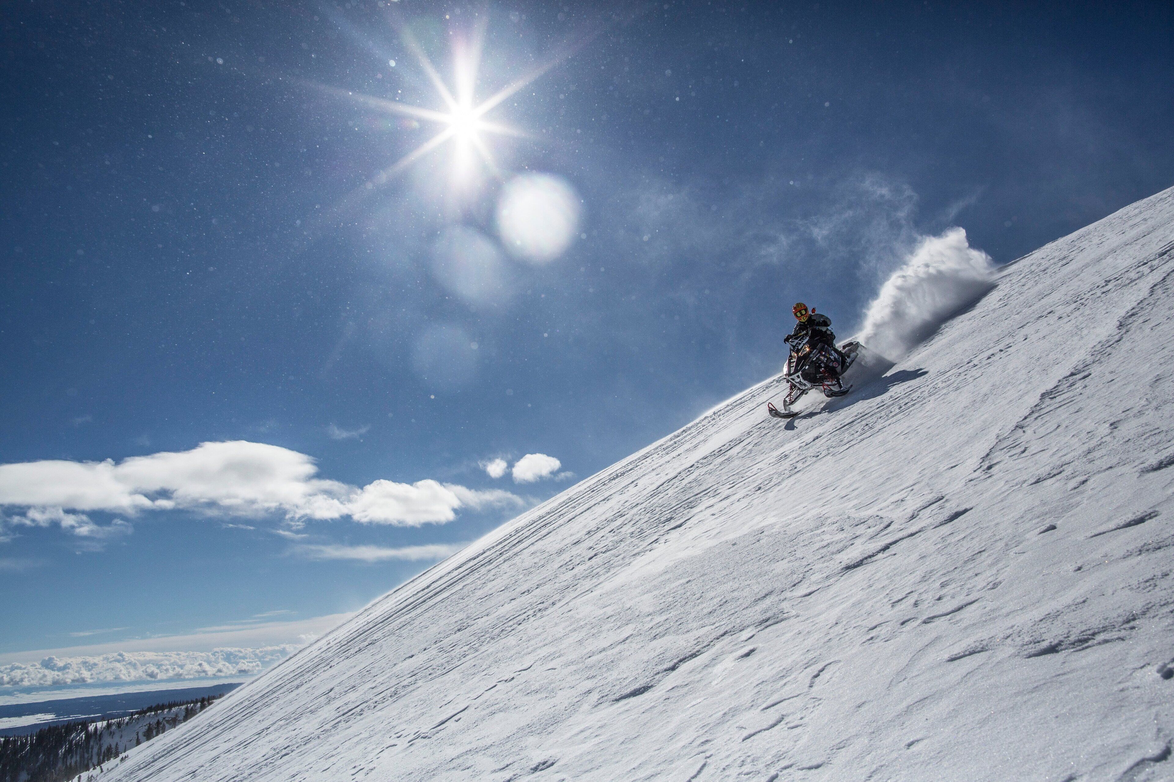 Ein mit Schnee bedeckter Hang, auf dem eine Person einen Schneemobil fährt.