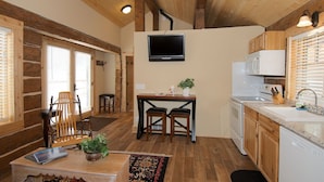 A compact kitchen with a TV, wooden cabinets, and a dining area with a chair and table. - True Grit Adventure (Island Park)