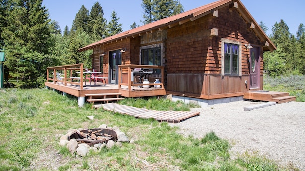 A rustic cabin with a deck, a fire pit, and a view of the surrounding forest. - True Grit Adventure (Island Park)