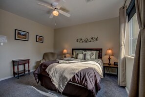 A bedroom with a bed, two bedside tables with lamps, a chair, a ceiling fan, and two framed pictures on the wall. - Pecan Point (Hurricane)