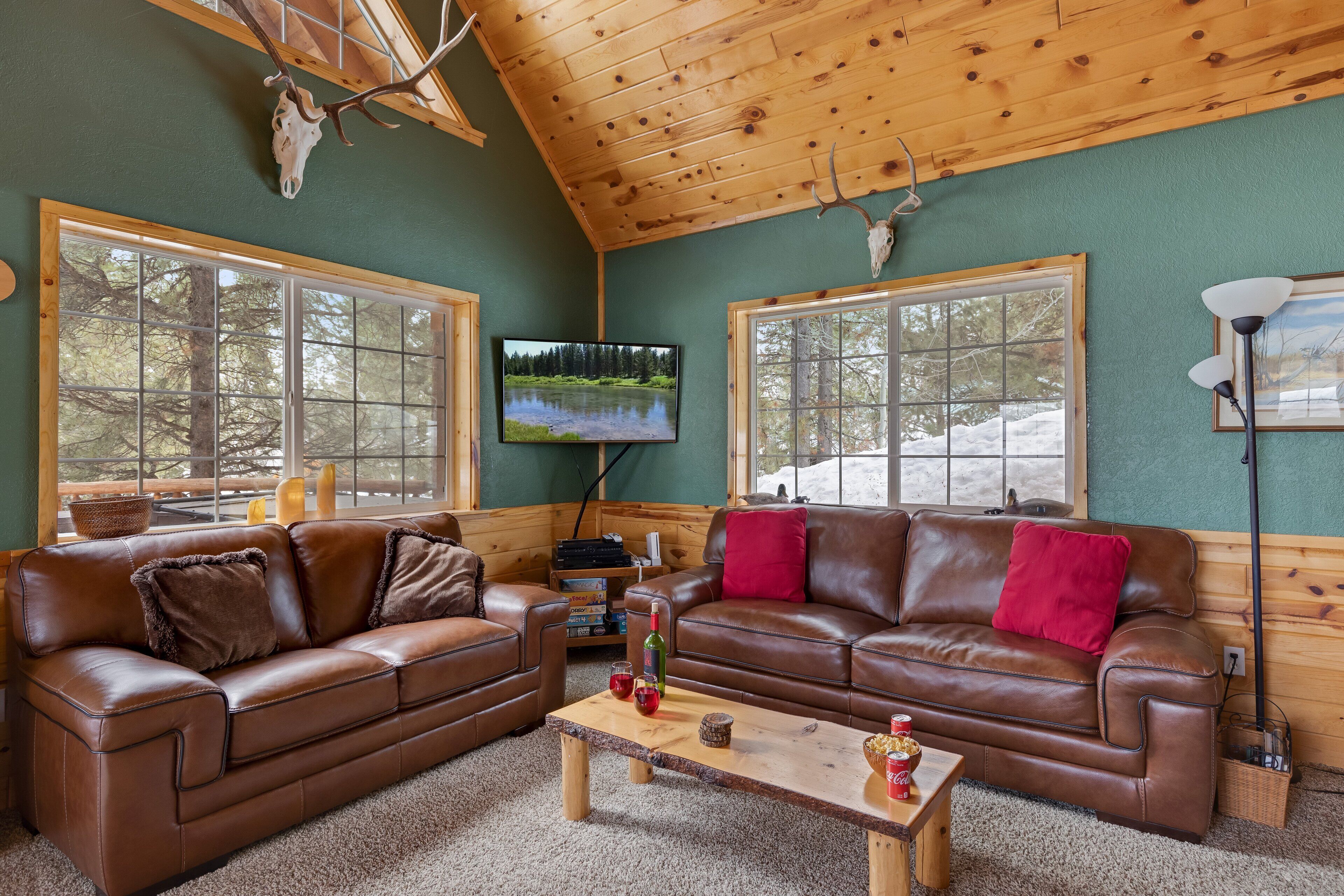 L’intérieur chaleureux d’un chalet avec deux canapés en cuir, une table basse en bois et un téléviseur fixé au mur.