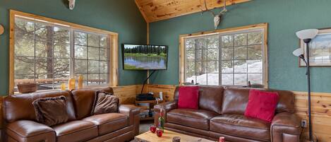 L’intérieur chaleureux d’un chalet avec deux canapés en cuir, une table basse en bois et un téléviseur fixé au mur.