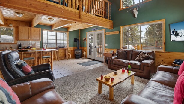 A spacious cabin with a high ceiling, wooden interior, a dining area, and a cozy living room with leather furniture.