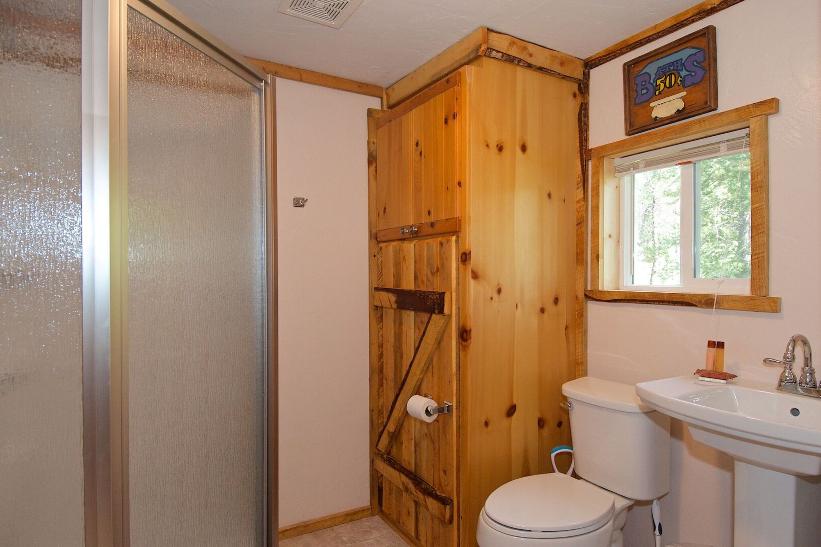 Un baño con puerta de madera, inodoro, lavamanos y ventana.