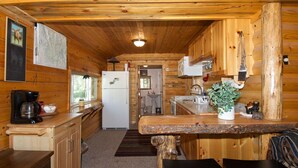 A wooden cabin interior with a kitchen, dining area, and a bathroom visible through an open door. - Remington Retreat (Island Park)