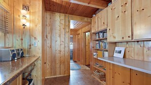 A wooden interior with a kitchen area, bar stools, and a bookshelf. - Restoration Pines (Island Park)