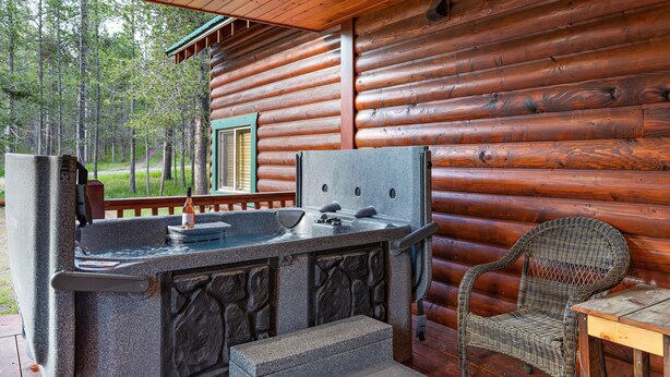 A wooden cabin with a stone bar area, a wicker chair, and a view of the forest. - Restoration Pines (Island Park)