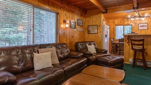 A cozy cabin interior with a leather sofa, a wooden dining table, and a bar area. - Restoration Pines (Island Park)