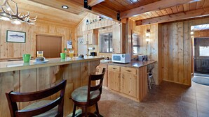 A wooden cabin kitchen with a bar area, wooden cabinets, and a deer antler chandelier. - Restoration Pines (Island Park)