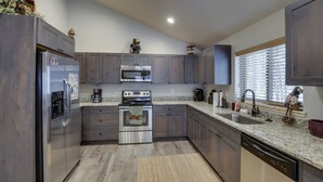A modern kitchen with dark wood cabinets, stainless steel appliances, a granite countertop, and a window with blinds. - Buck Buck Moose (Island Park)