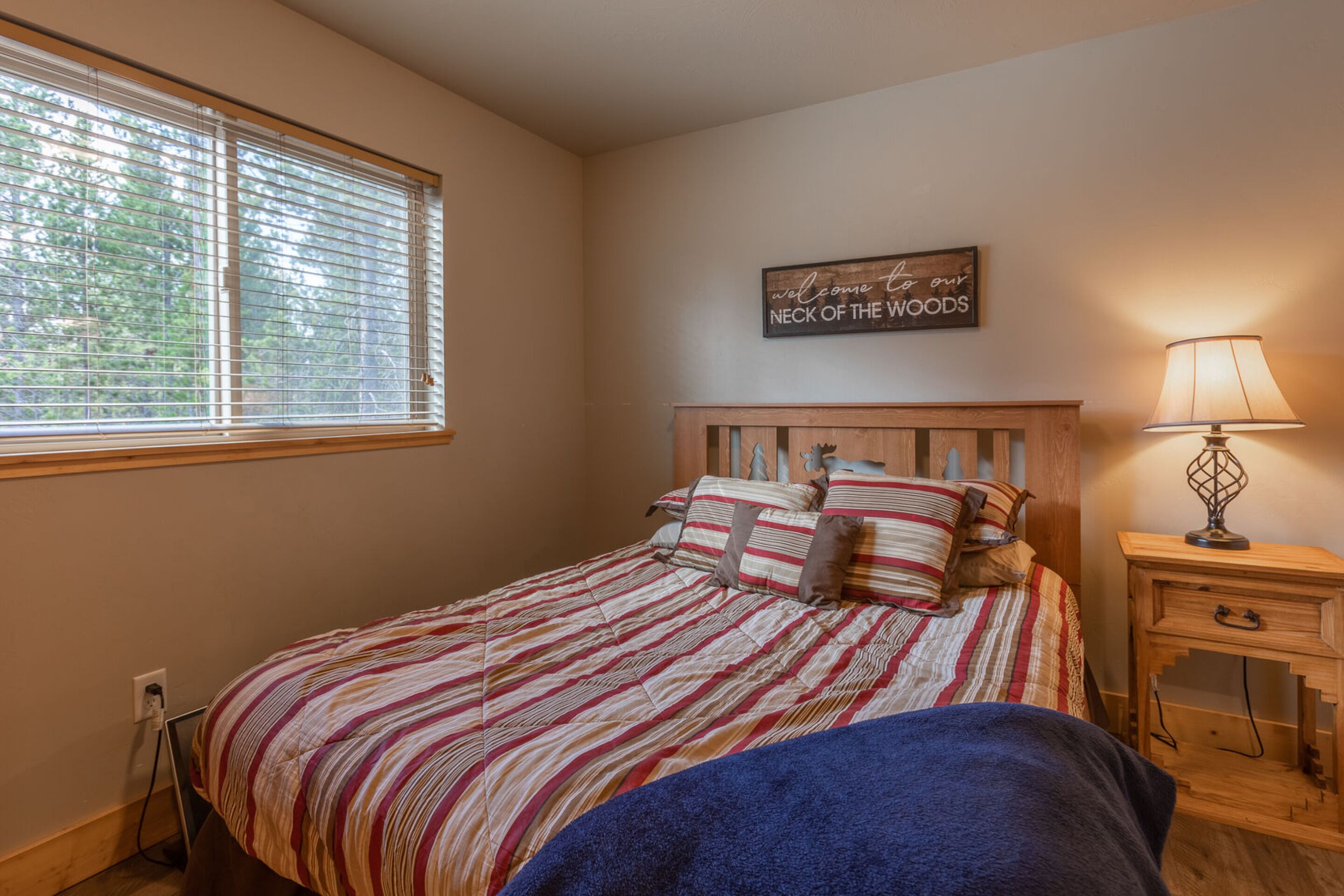 A bedroom with a bed, a bedside table, a lamp, and a window with blinds.