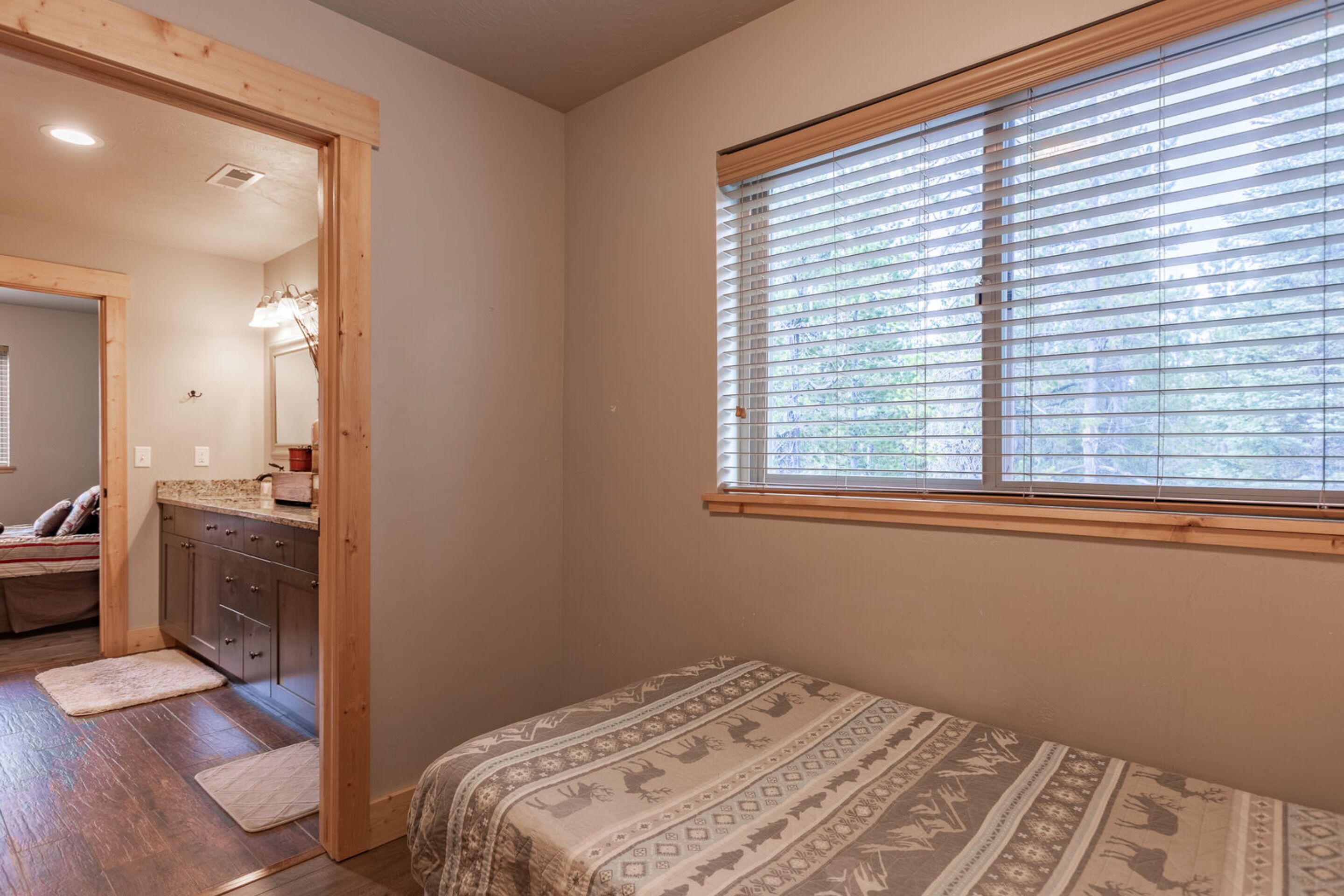 Une chambre avec un lit, une fenêtre avec des stores, une porte en bois et une petite kitchenette.