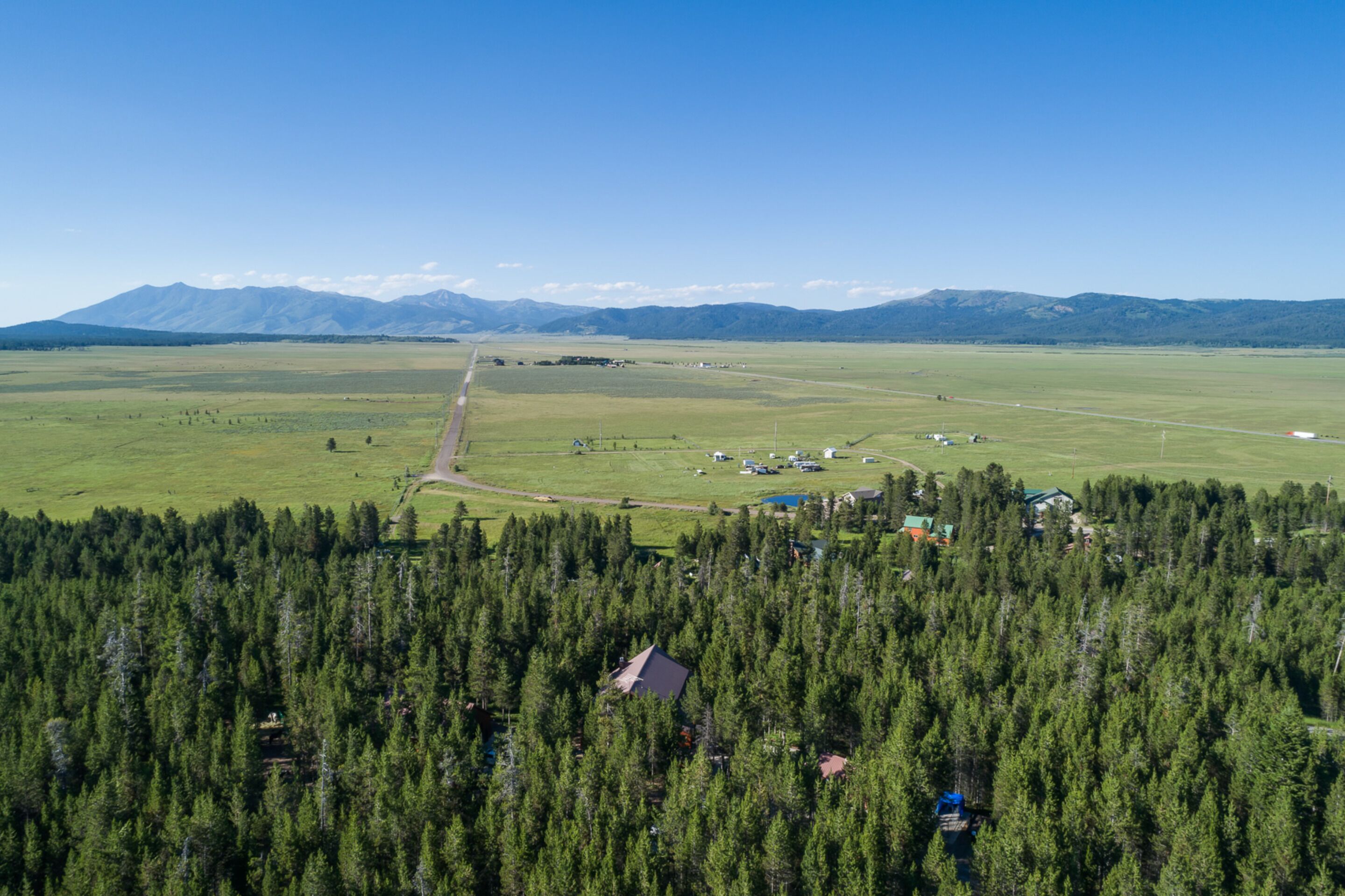 An aerial view of a rural area with a road, a small settlement, and a dense forest.