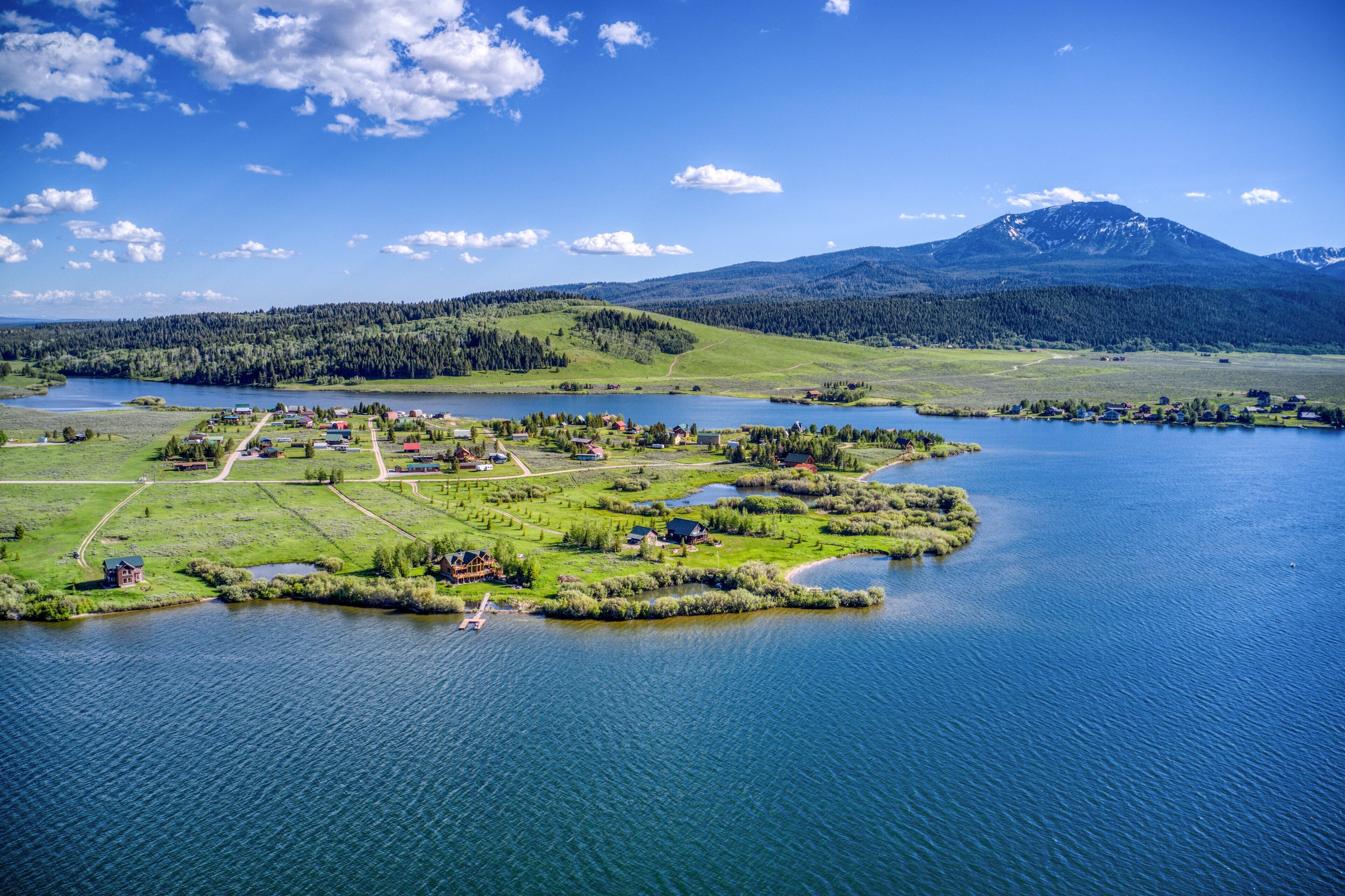 An aerial view of a lakeside village with houses, paths, and a mountain in the background.