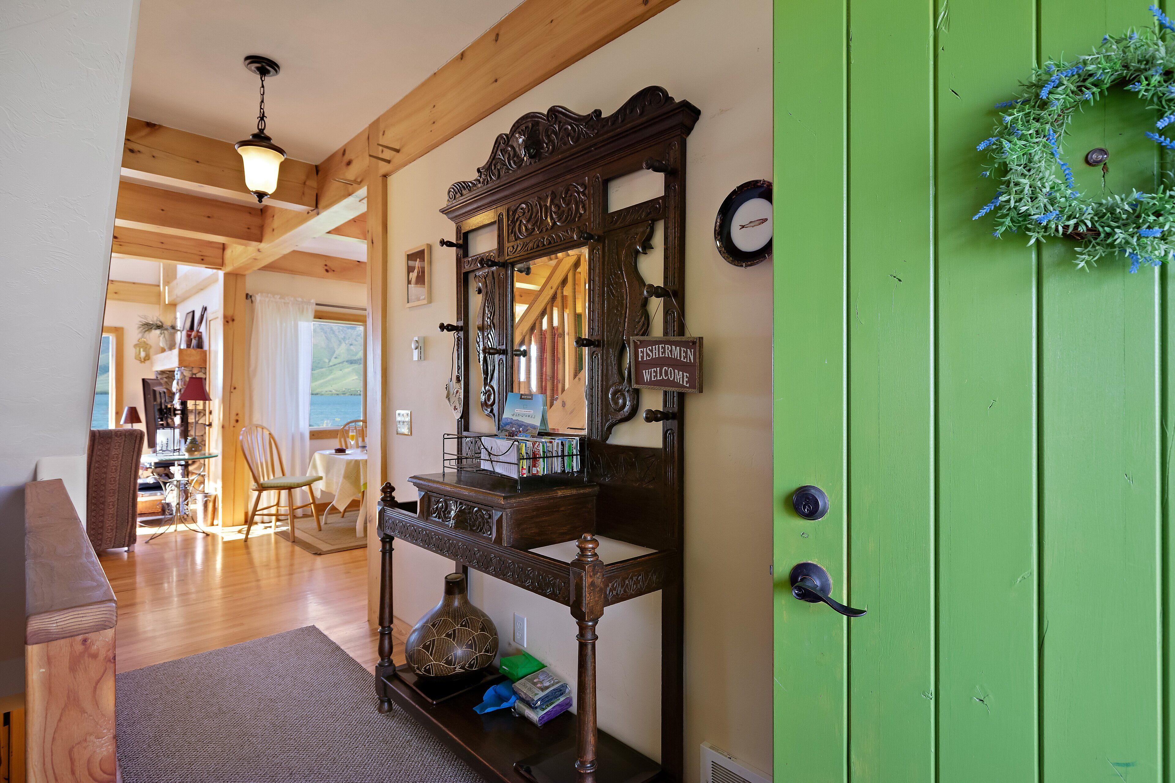 A wooden interior with a green door, a mirror, a welcome sign, and a view of the outdoors.