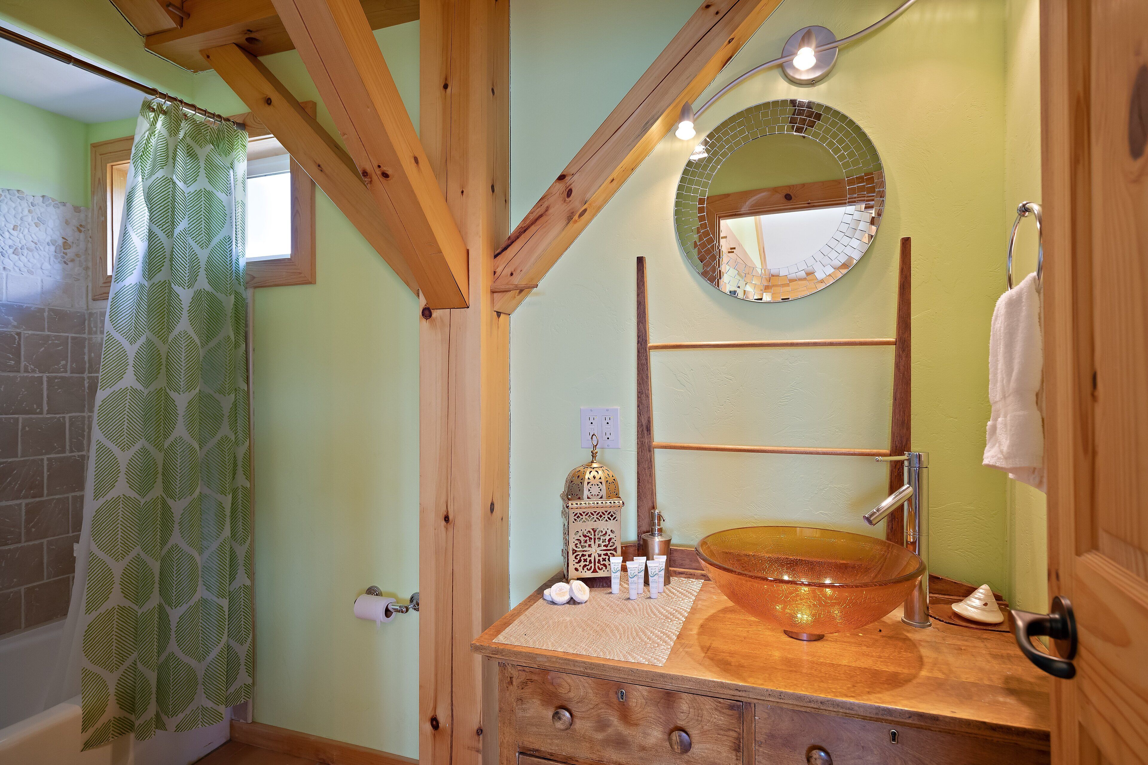A bathroom with a wooden vanity, a glass bowl sink, a mirror, and a shower curtain.